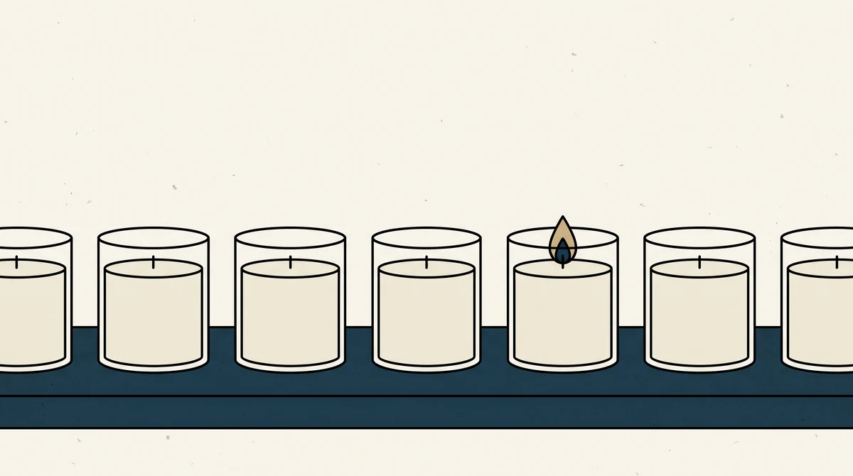 A row of poured candles in plain glass jars on a shelf, one lit and the rest unlit.